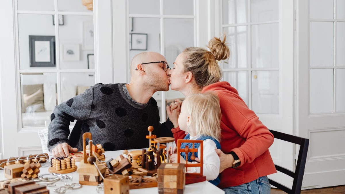 A family shares a loving moment indoors, surrounded by wooden toys, depicting warmth and togetherness.